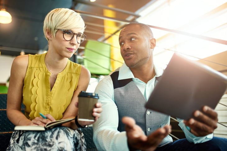 Two creative millenial small business owners working on an AI ecommerce strategy using a digital tablet while sitting in staircase